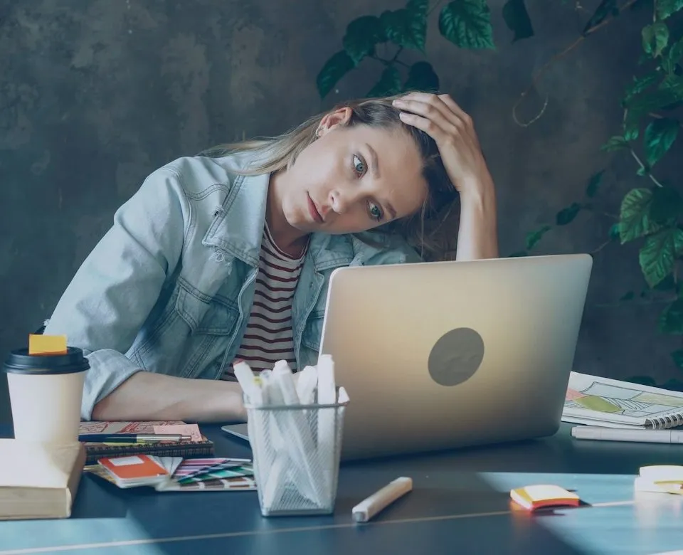 Une personne épuisée, la main dans les cheveux, face à son ordinateur au bureau